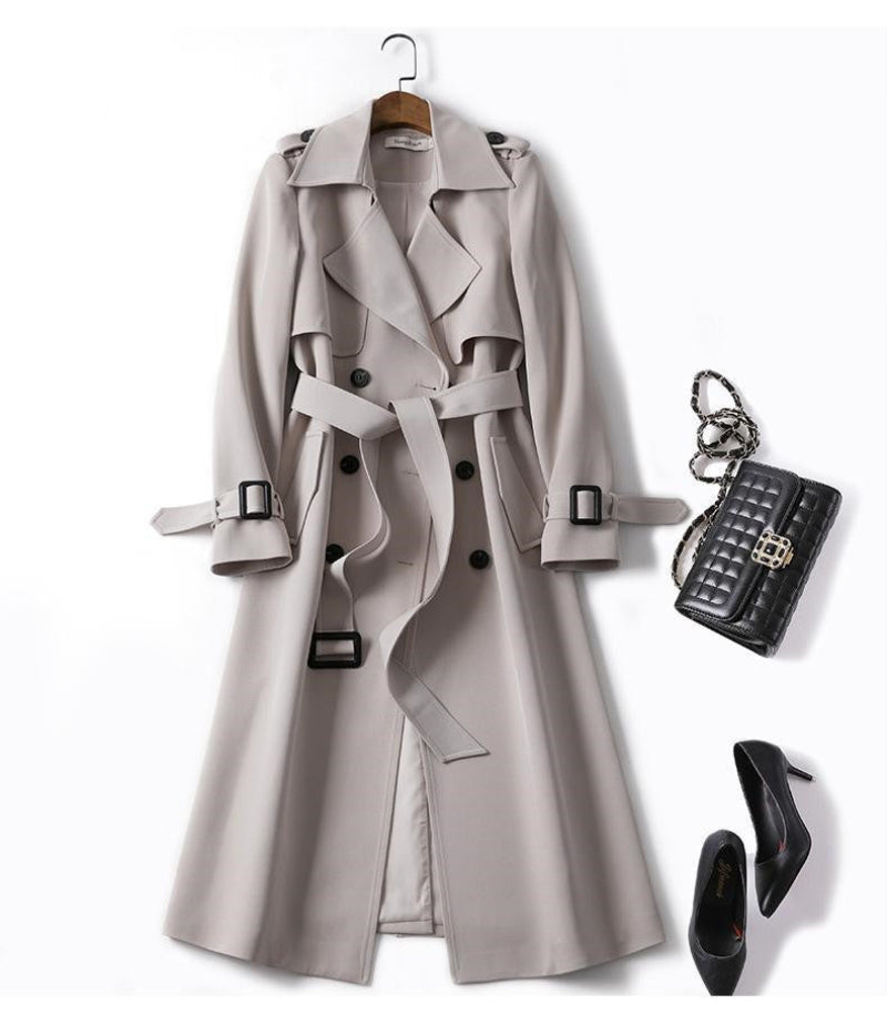 Gray trench coat with black shoes, handbag, and keychain on a white background