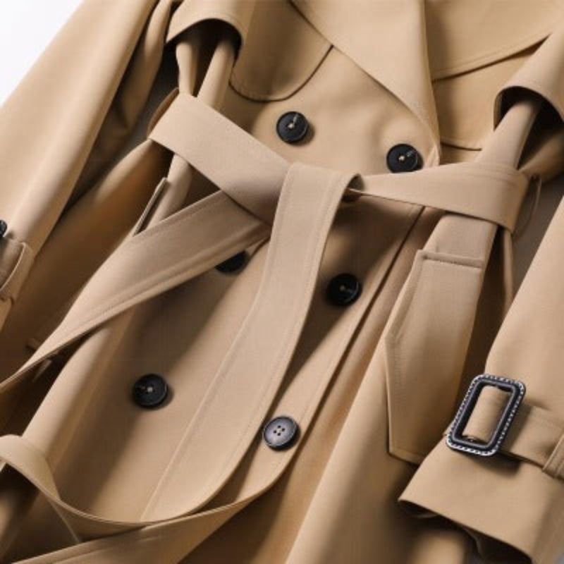 Close-up of a beige trench coat with black buttons and a decorative buckle.