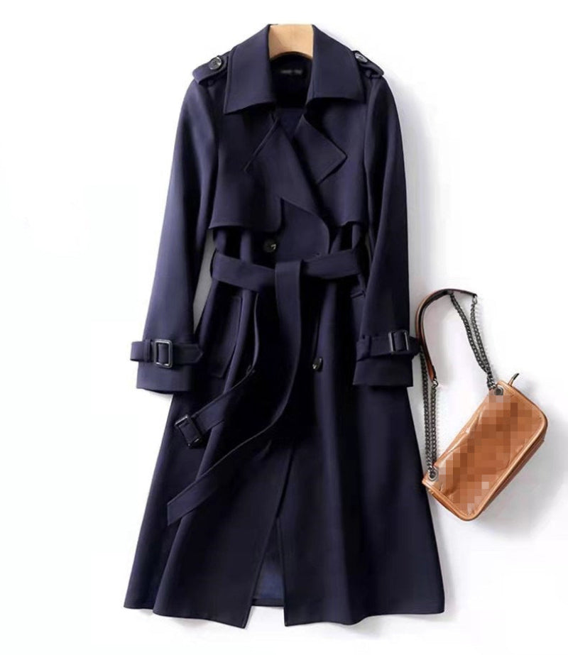 Navy blue trench coat on a hanger with a wooden handbag beside it on a white background
