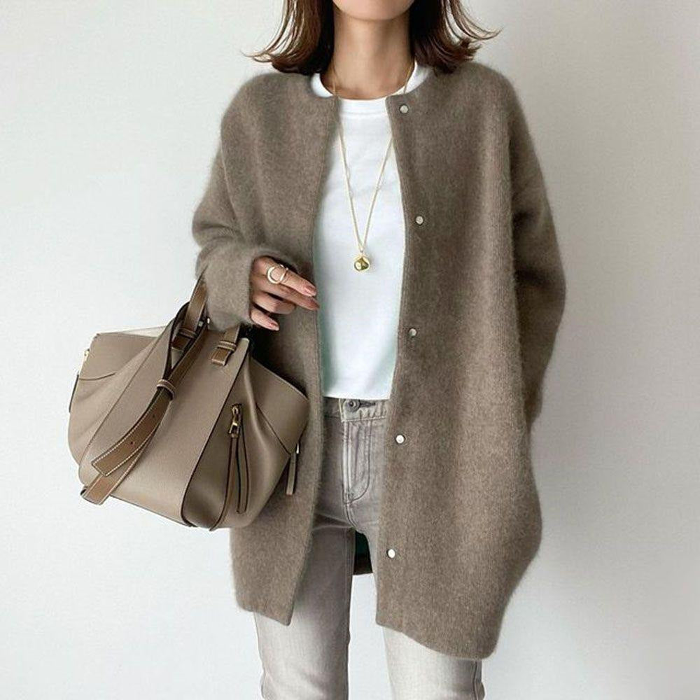 Person wearing a brown cardigan holding a beige handbag on a plain background
