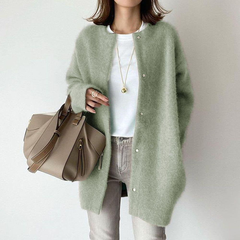 Person wearing a green cardigan holding a beige handbag on a plain background