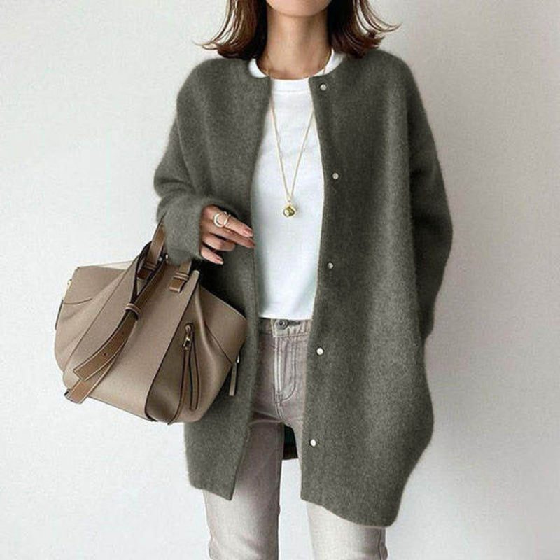 Person wearing a gray cardigan, white shirt, and beige pants holding a beige handbag against a plain background