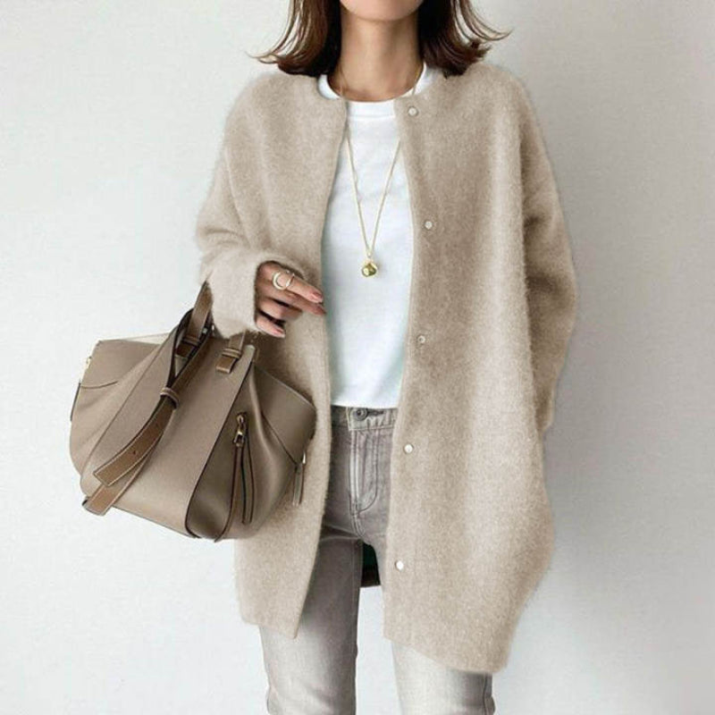 Person wearing a beige cardigan holding a matching handbag against a plain background